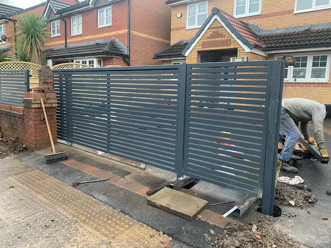 Grey horizontal slatted driveway gates being installed